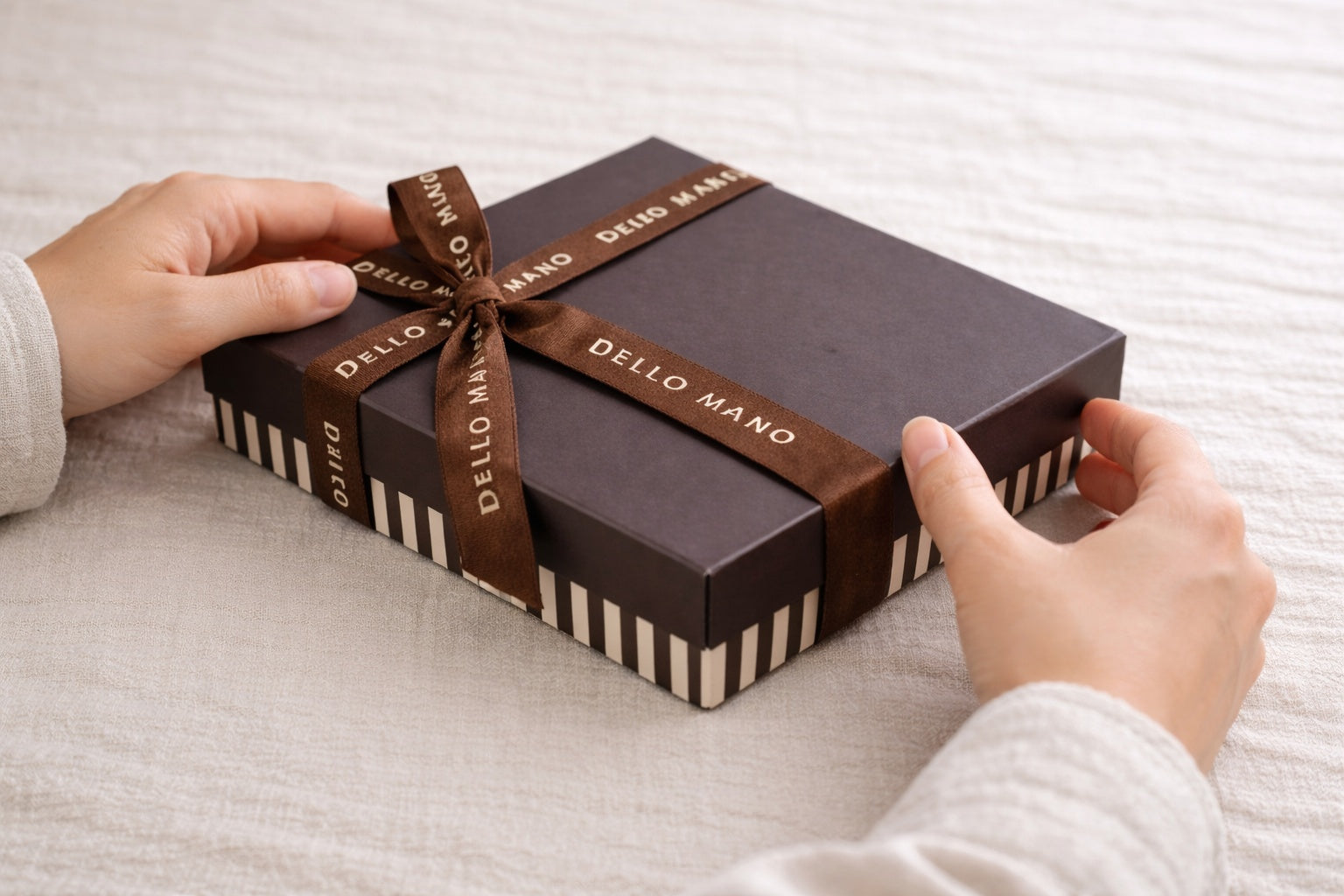 Hands adjusting a handmade Dello Mano gift box on a soft linen surface, reflecting thoughtful gift selection