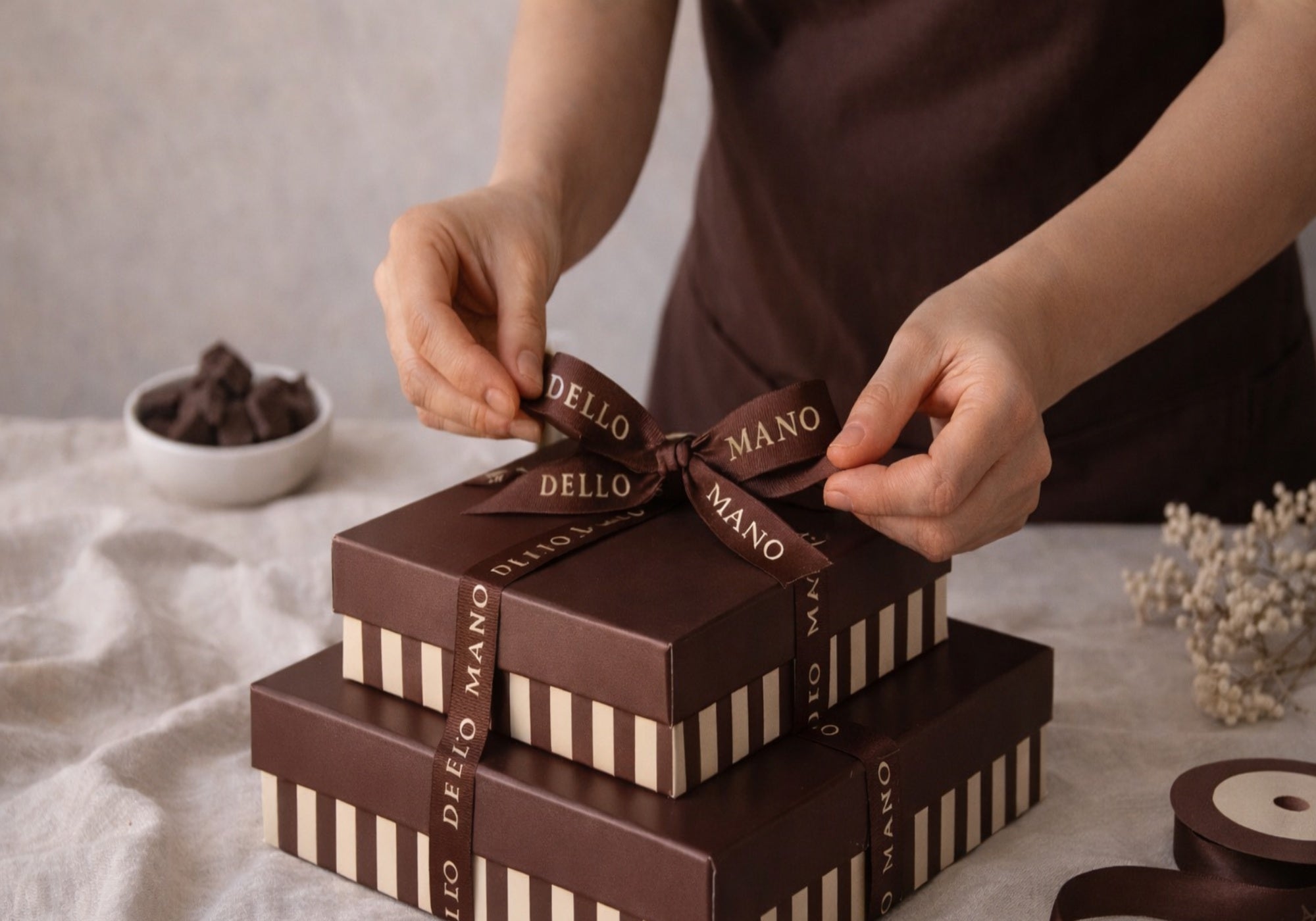 Hands tying ribbon on a Dello Mano chocolate gift box, showcasing handmade craftsmanship and small batch preparation