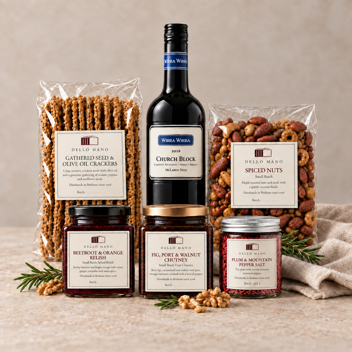 Five Dello Mano cheese-board foods arranged with rosemary and walnuts in front of a 2018 Wirra Wirra Church Block wine bottle.