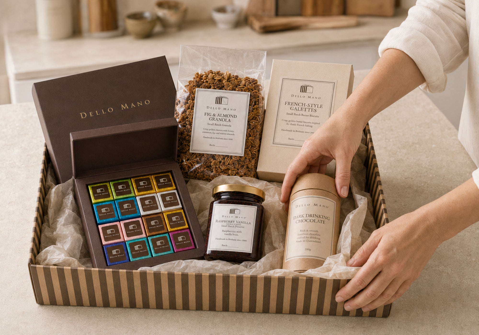 Dello Mano corporate hamper being packed by hand with brownies, granola, galettes, preserve and drinking chocolate in a striped kraft box.