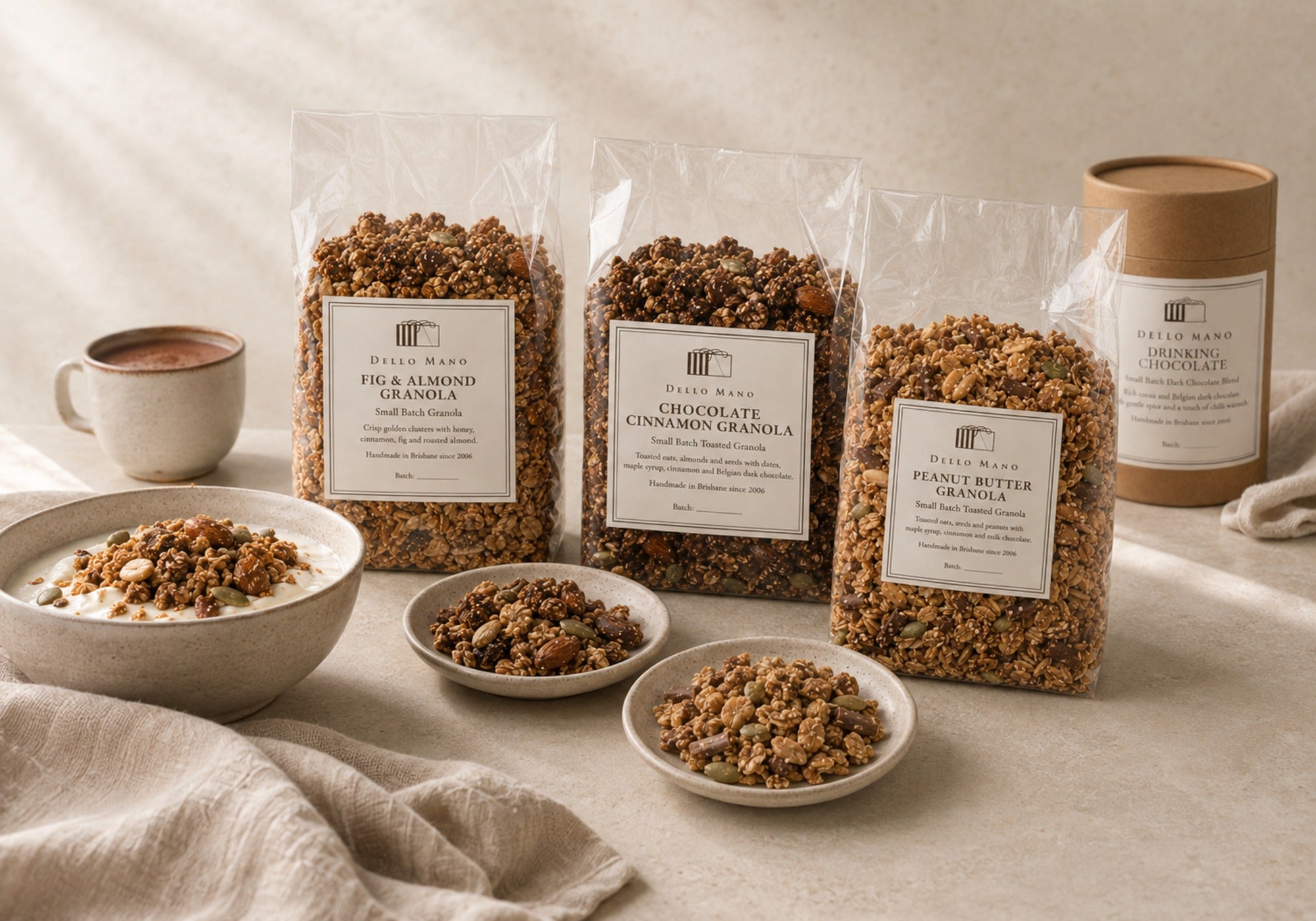 Three Dello Mano granolas presented with yoghurt and Dark Drinking Chocolate in a calm breakfast setting.
