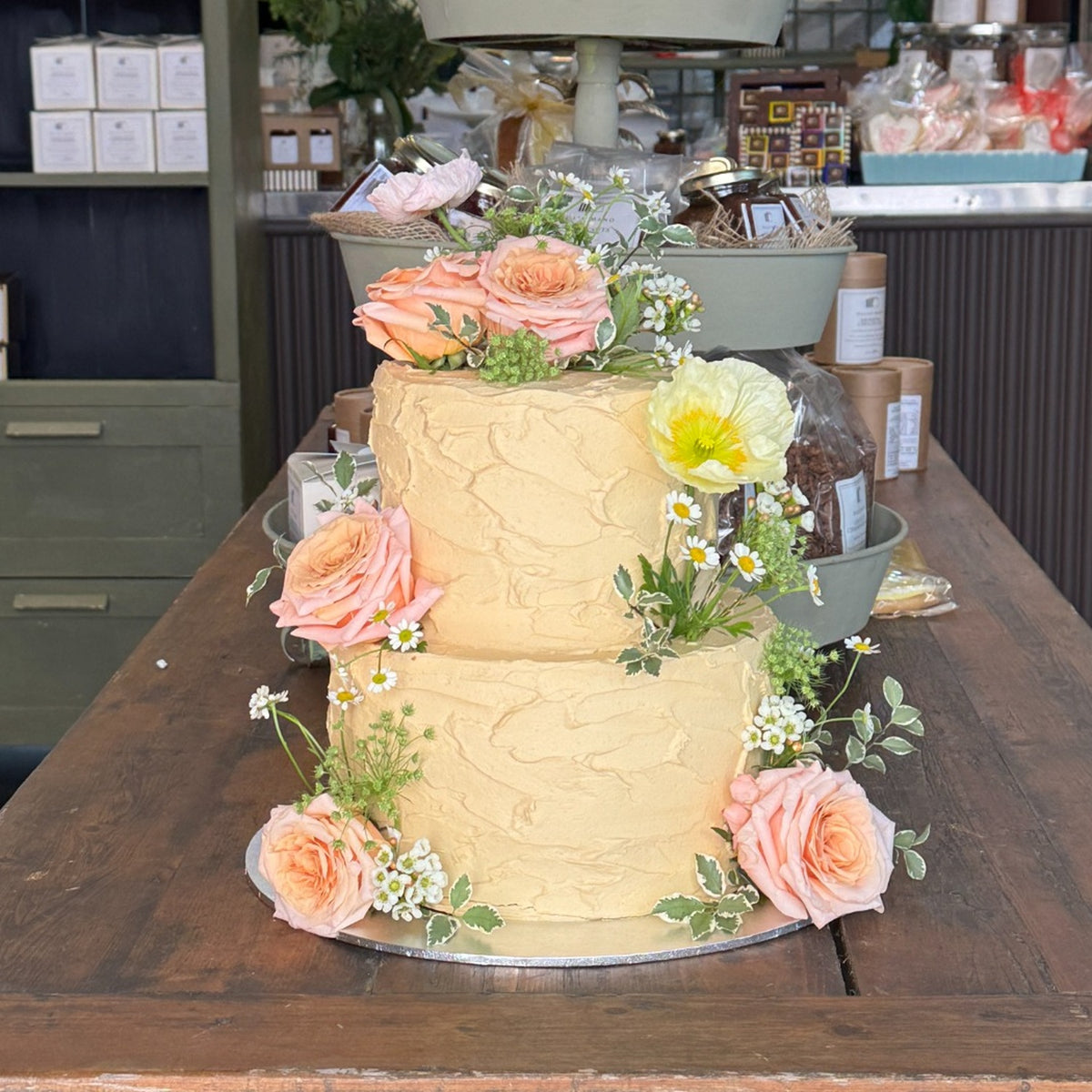 Caramel, Cream and Blossom two-tier Dello Mano celebration cake decorated with peach roses and seasonal flowers in the Brisbane store.