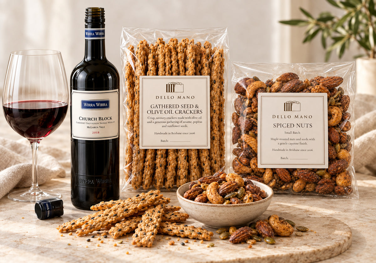 Dello Mano seeded crackers and spiced nuts beside an open bottle of 2018 Wirra Wirra Church Block and a glass of red wine.