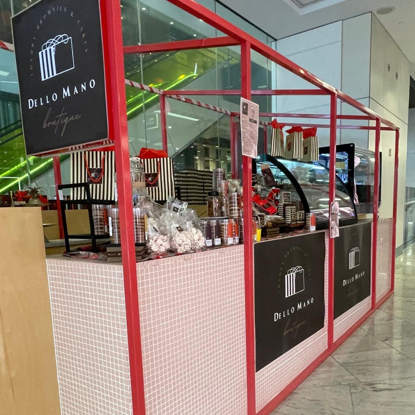 Dello Mano boutique kiosk inside a building with red frame and white checkered floor.
