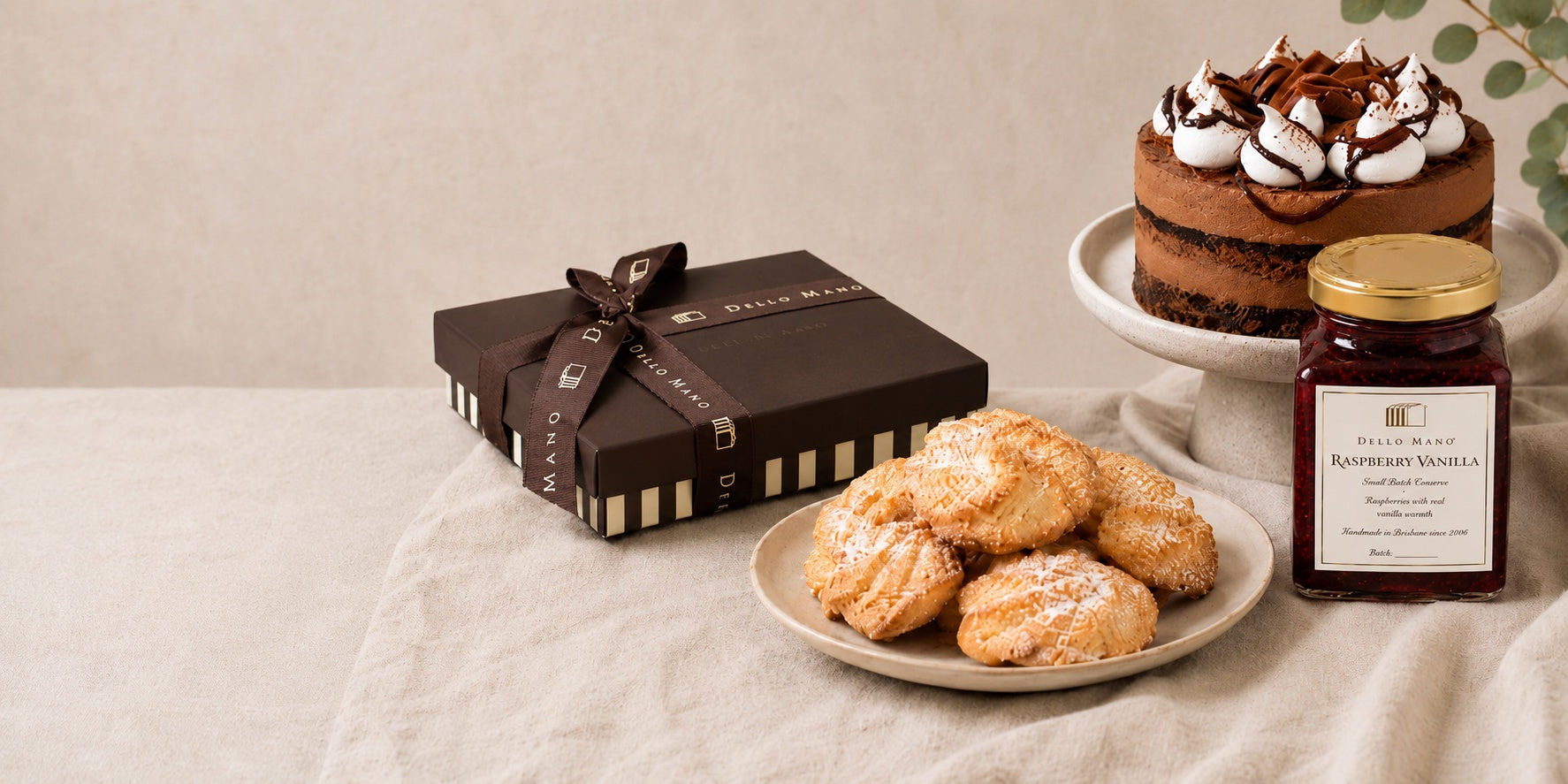 Dello Mano gift box, handmade biscuits, Raspberry Vanilla small-batch conserve and chocolate cake styled together on soft neutral linen.