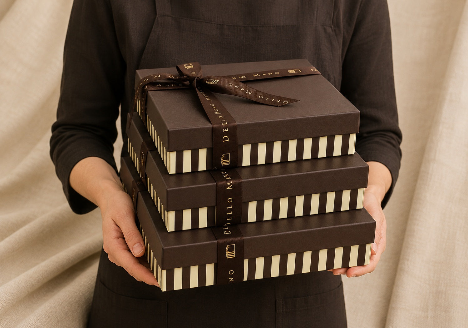 Dello Mano Extravagance Brownie Gift Box with three stacked luxury handmade brownie boxes tied with branded ribbon and held against a soft neutral linen backdrop.