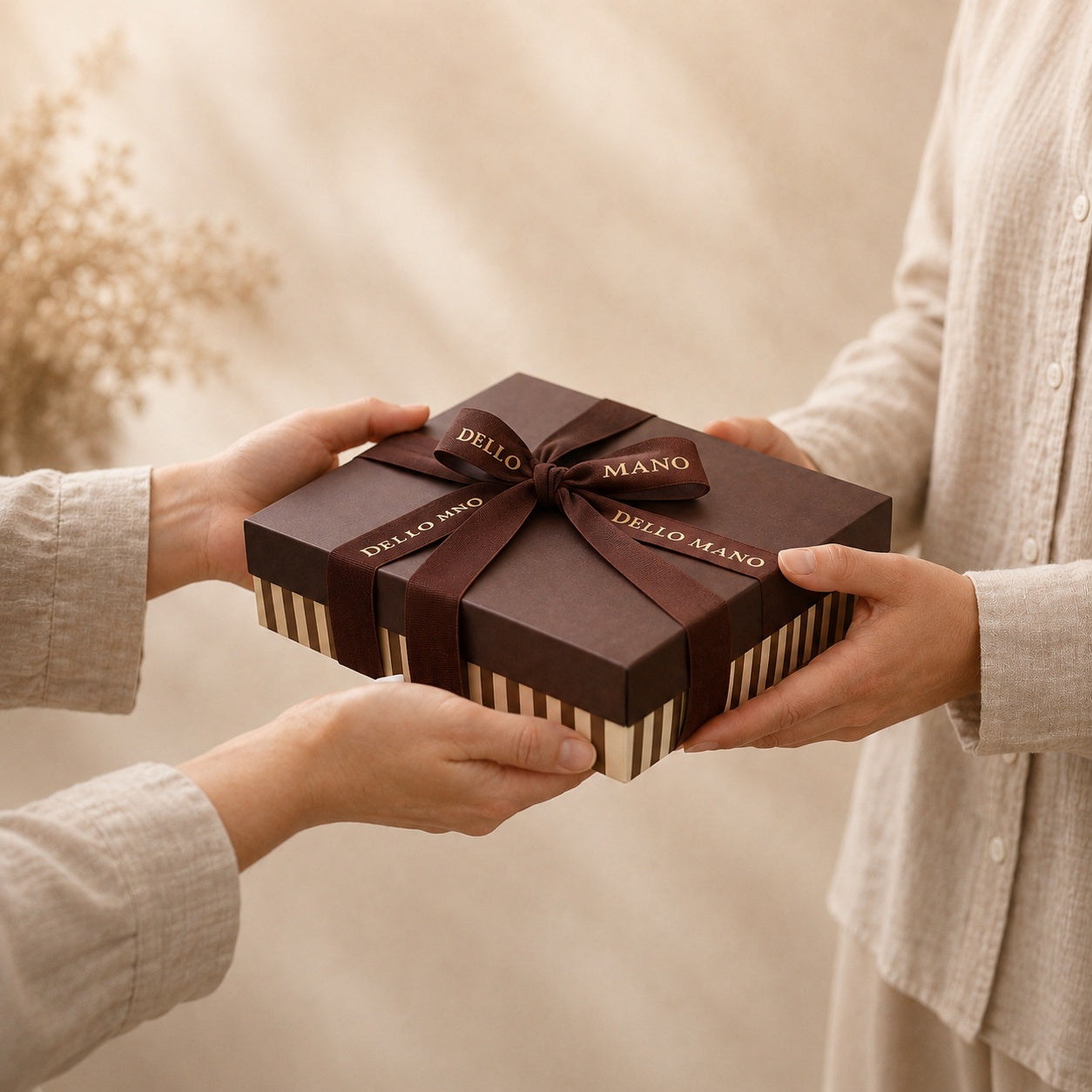 Dello Mano gift box tied with signature brown ribbon being exchanged between two people.