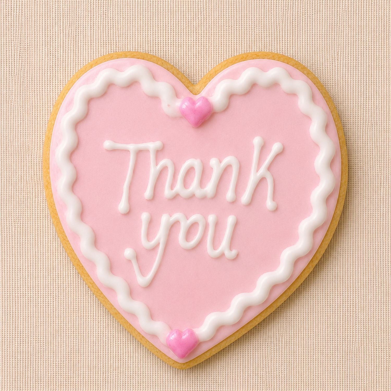 Pink heart-shaped iced thank you cookie with white piping detail on a soft neutral linen background.