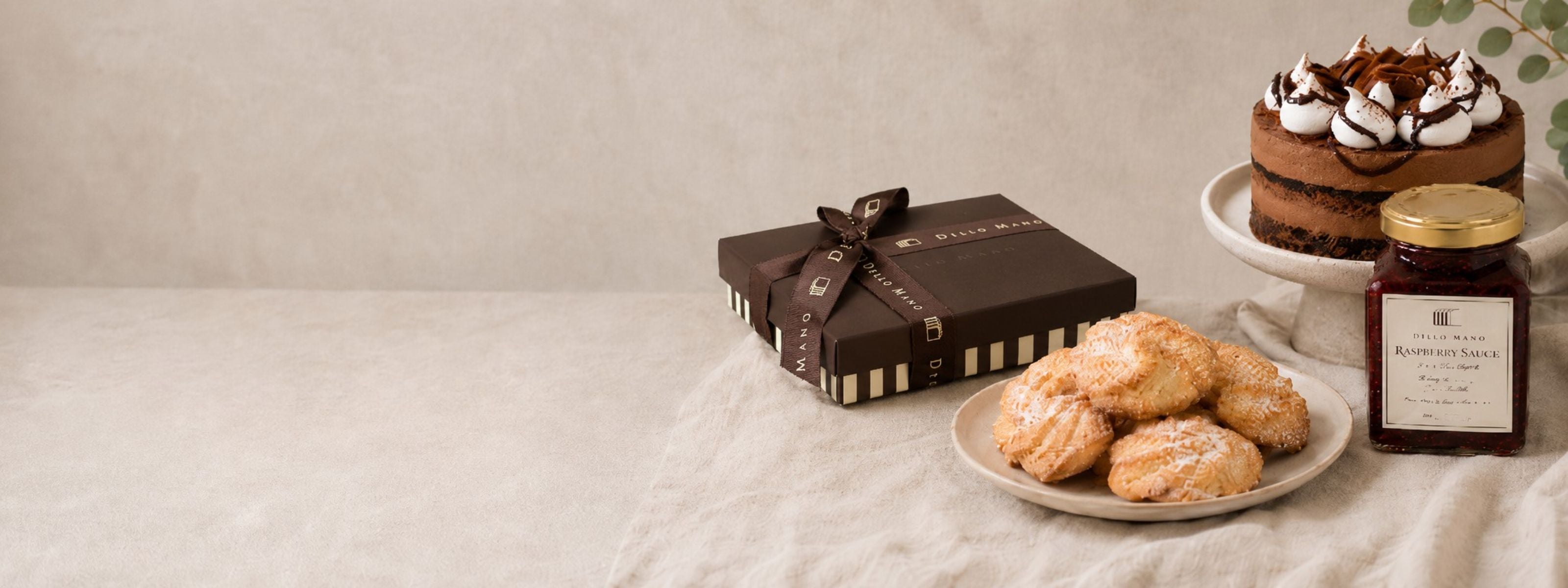 Dello Mano handmade gift box with chocolate cake, Danish butter biscuits and raspberry vanilla conserve styled on soft neutral linen.