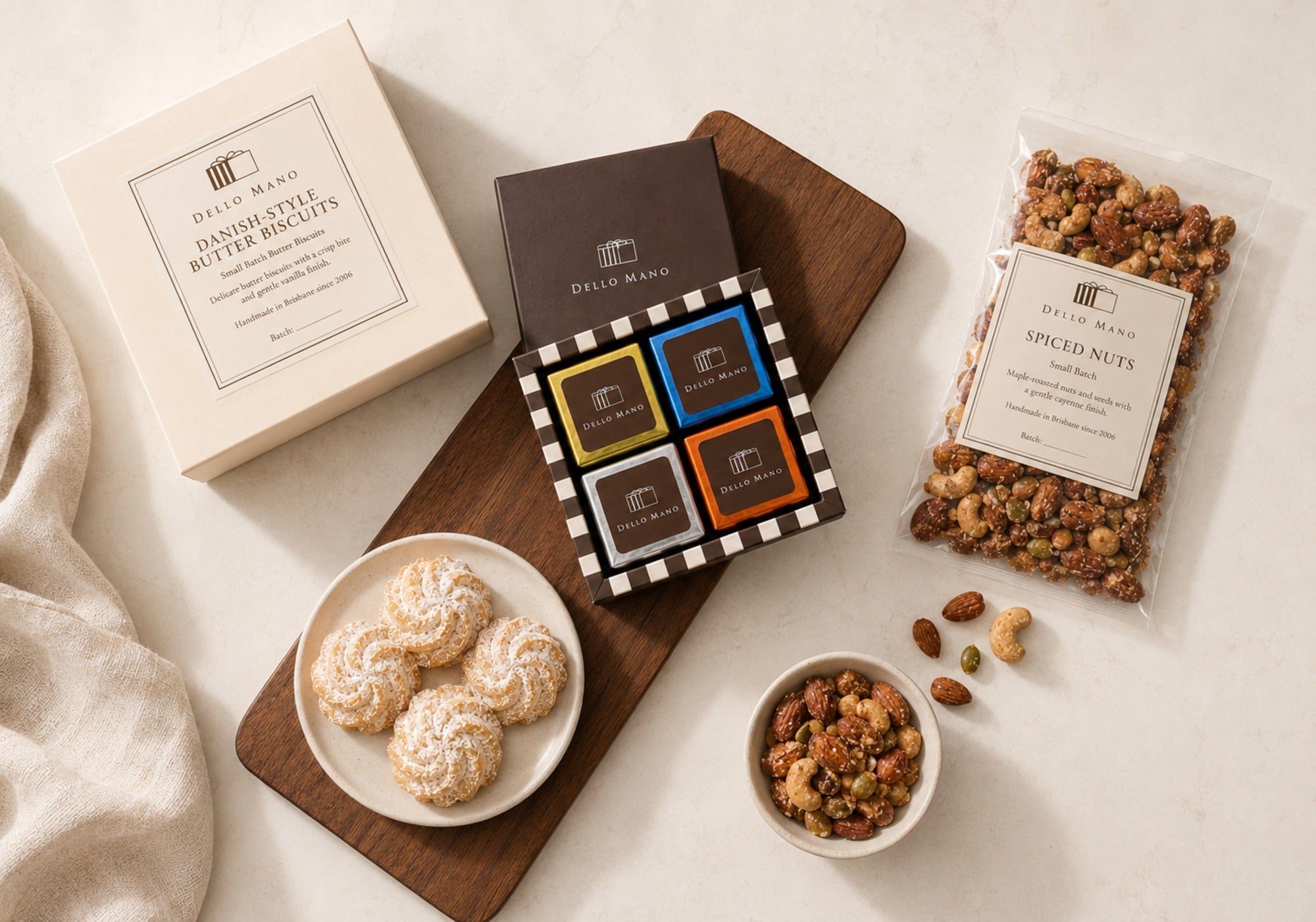 Overhead display of The Little Handmade Hamper contents with mixed brownies, Danish Butter Biscuits and labelled Dello Mano spiced nuts.