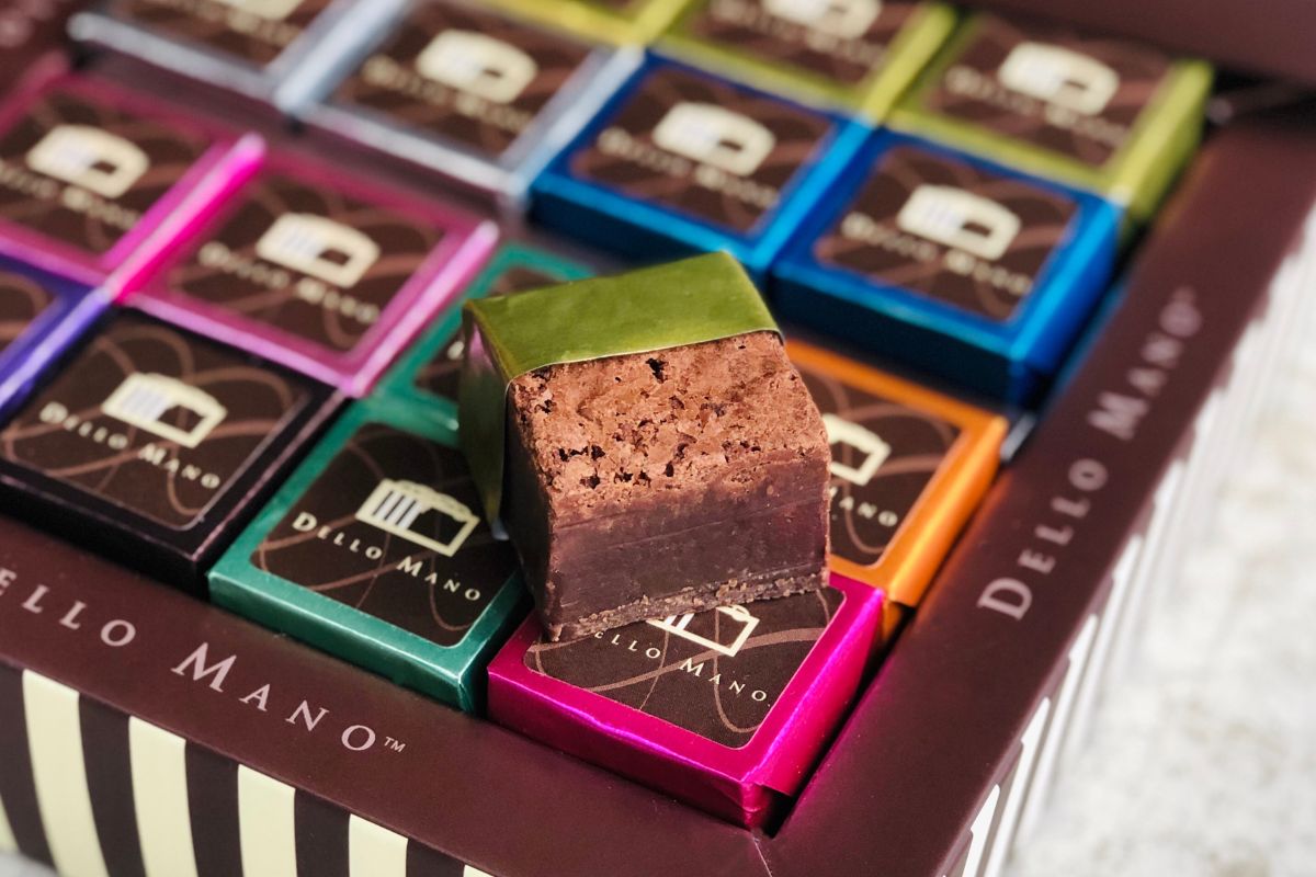 A Dello Mano brownie gift box filled with  colourful brownie cubes with one brownie open on top showing delicious fudgy texture.