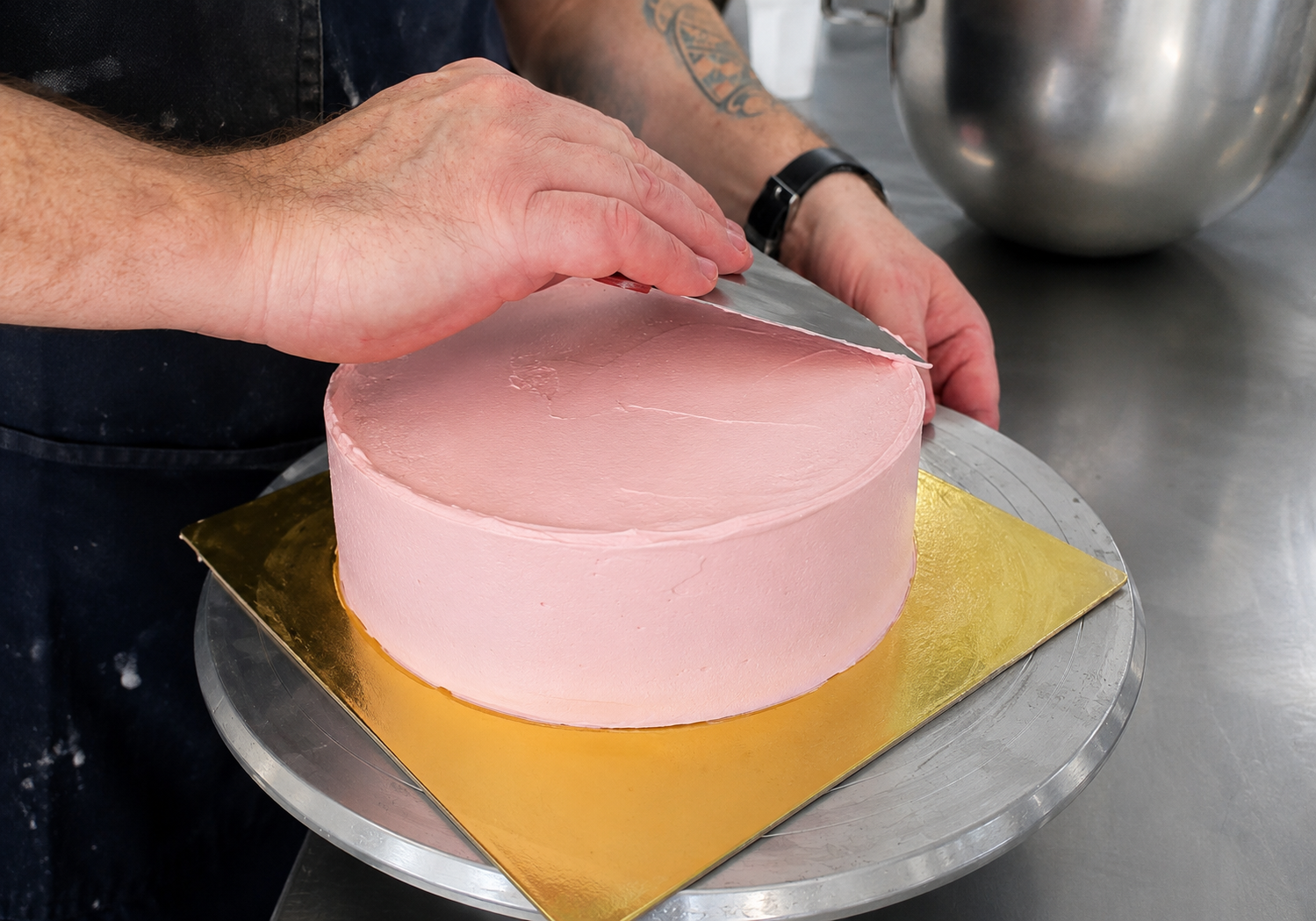 Dello Mano pastry chef smoothing pink frosting on a handmade cake in the Brisbane kitchen