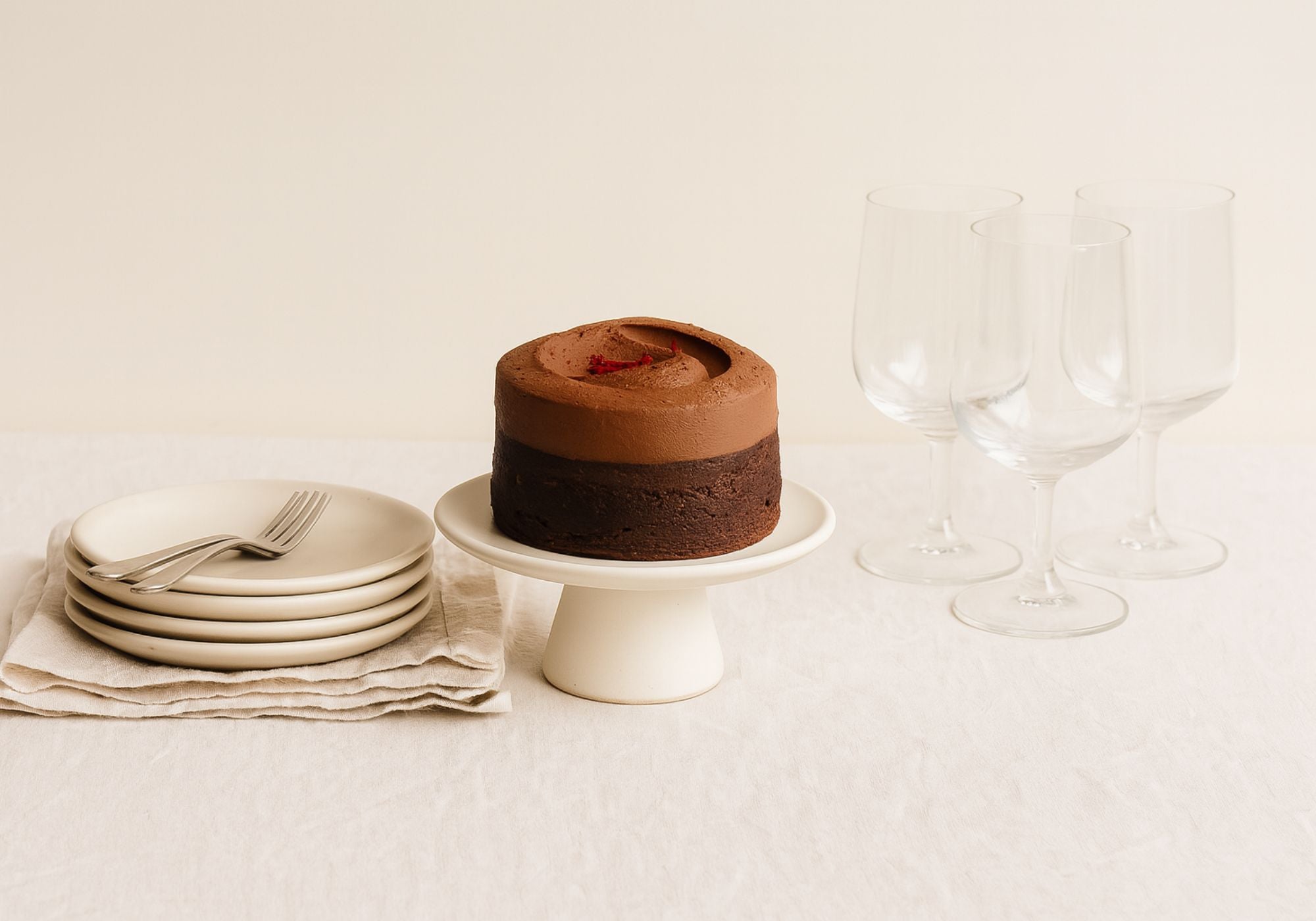 Small chocolate cake  that serves 4-6 on a white stand with four plates and four glasses on a light background