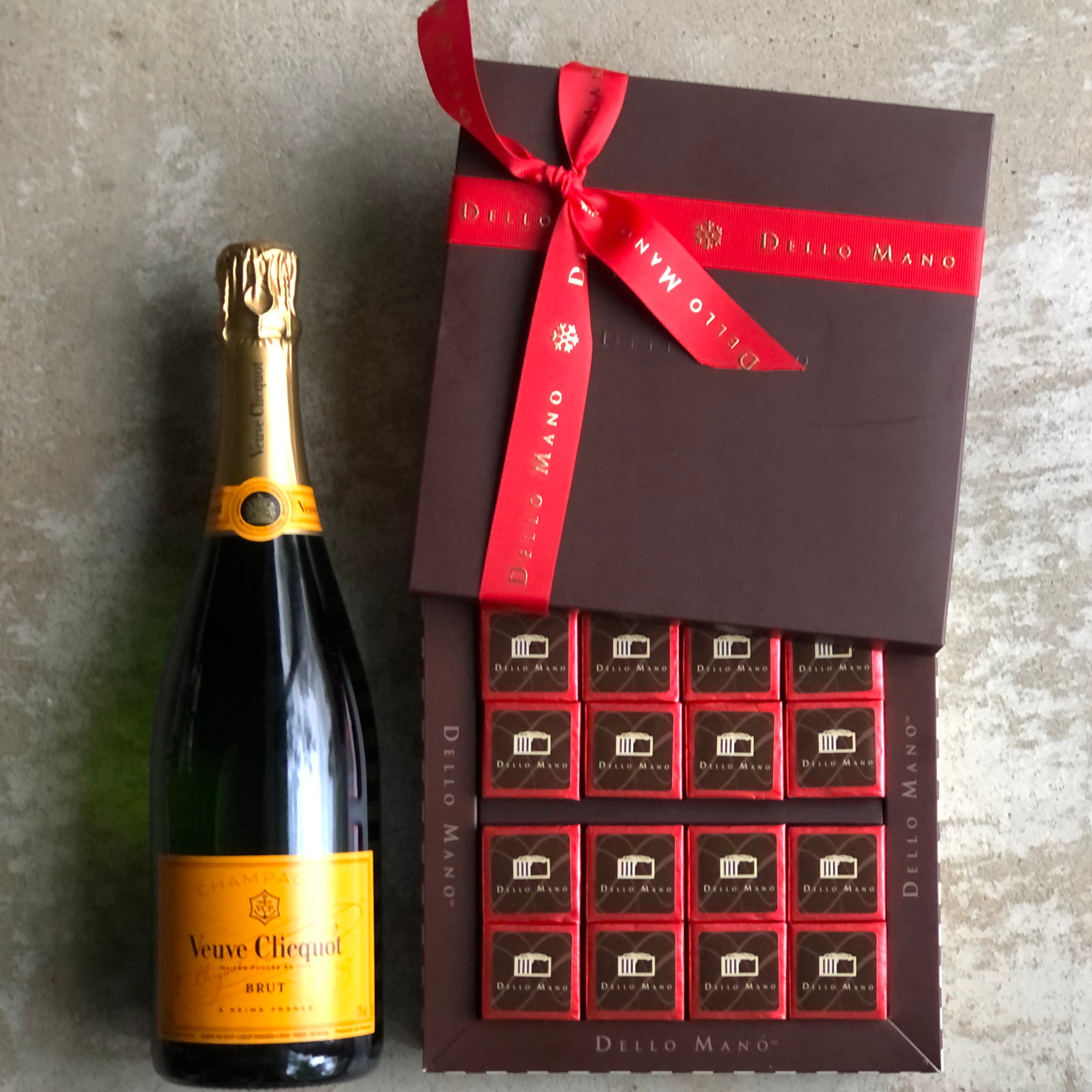 An open box of red foiled individually wrapped gluten free brownies in  a brown chocolate gift box. Beside the box is a bottle of Veuve cCiquot champagne.