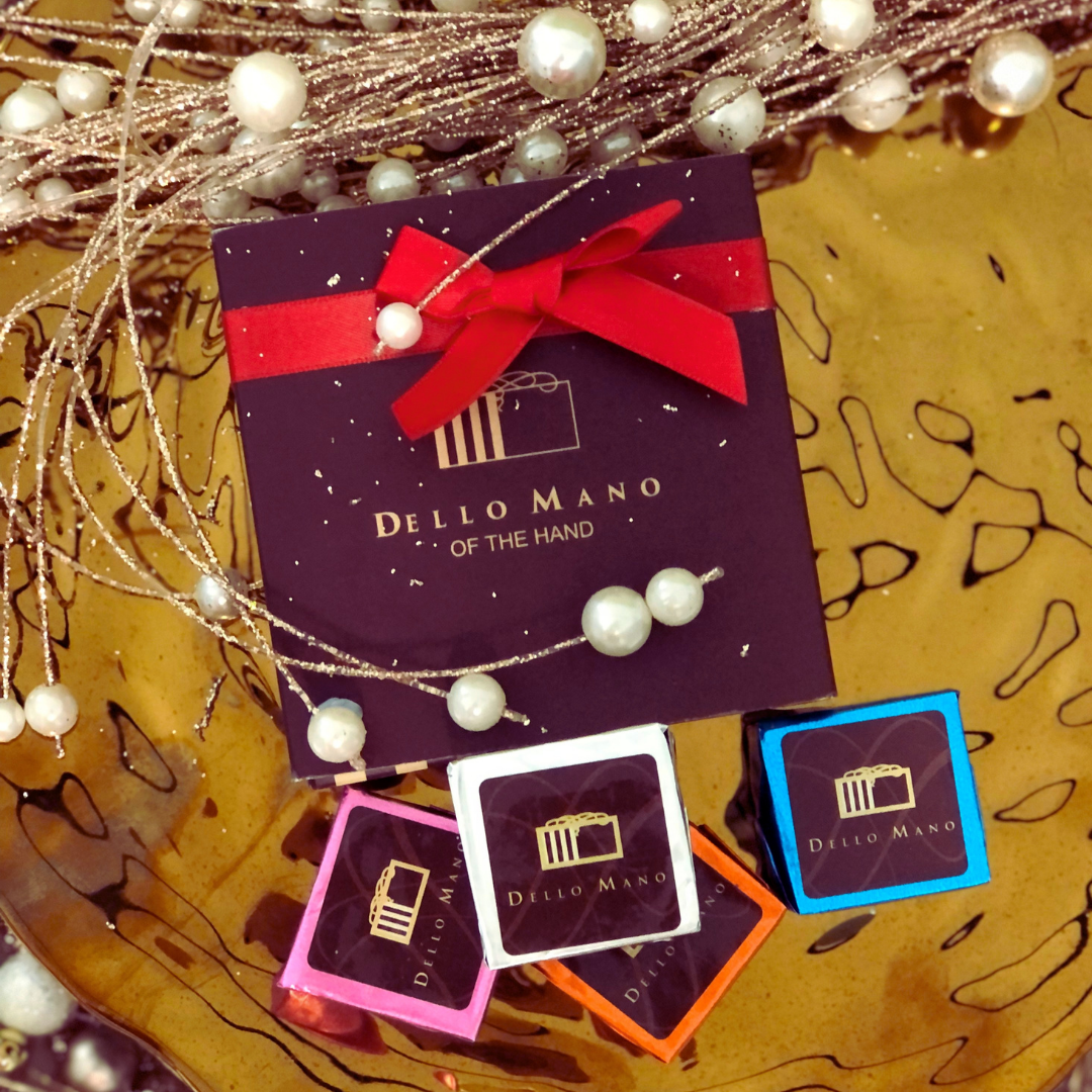 Dello Mano brownie gift box with red ribbon and four colourful treats styled among gold and pearl holiday décor.