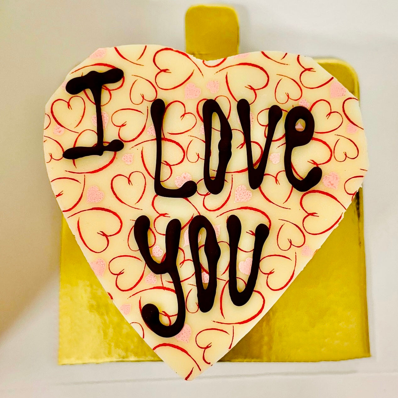 A brownie heart filled with chocolate buttercream and topped with white chocolate heart that says "I love you"