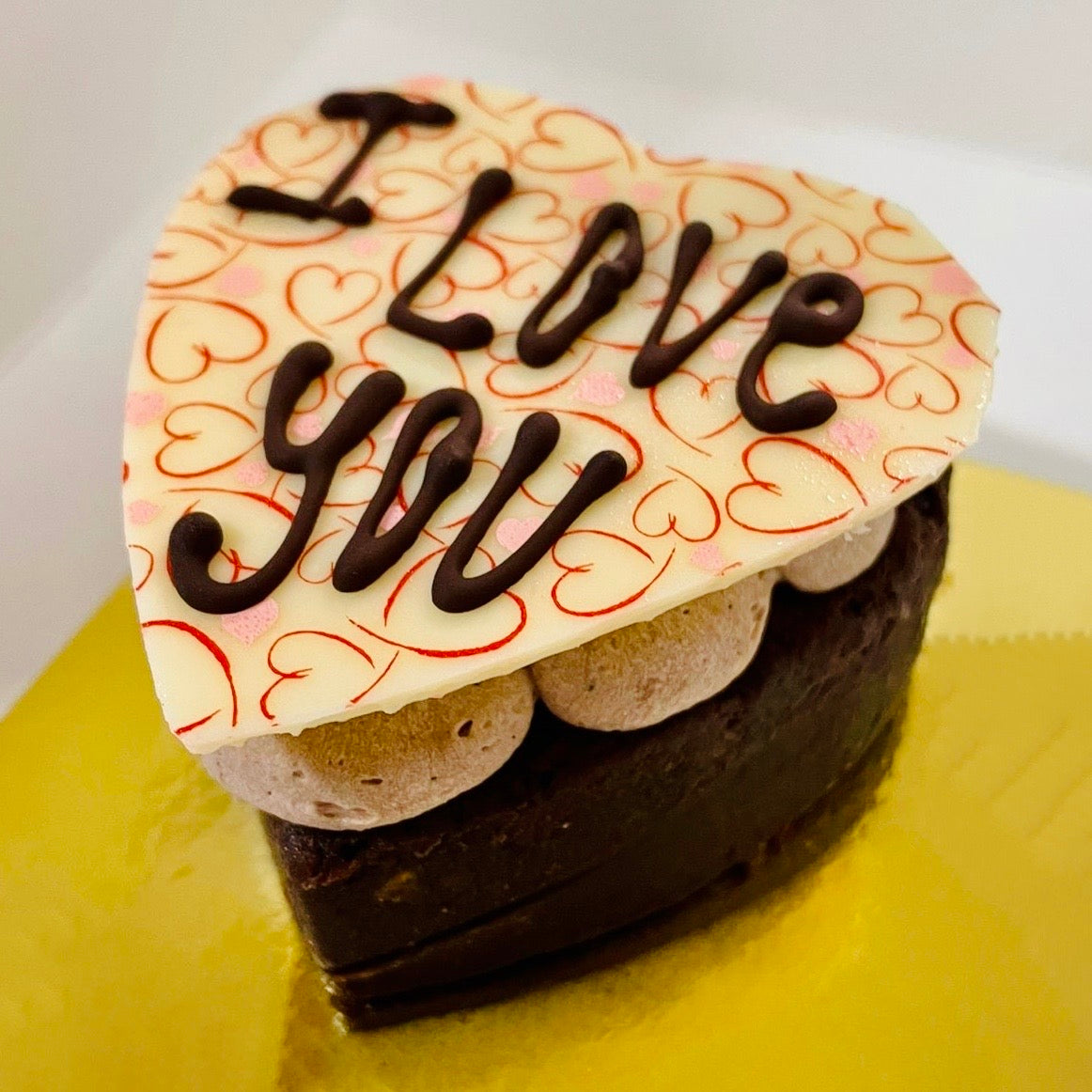 A brownie heart filled with chocolate buttercream and topped with white chocolate heart that says "I love you"