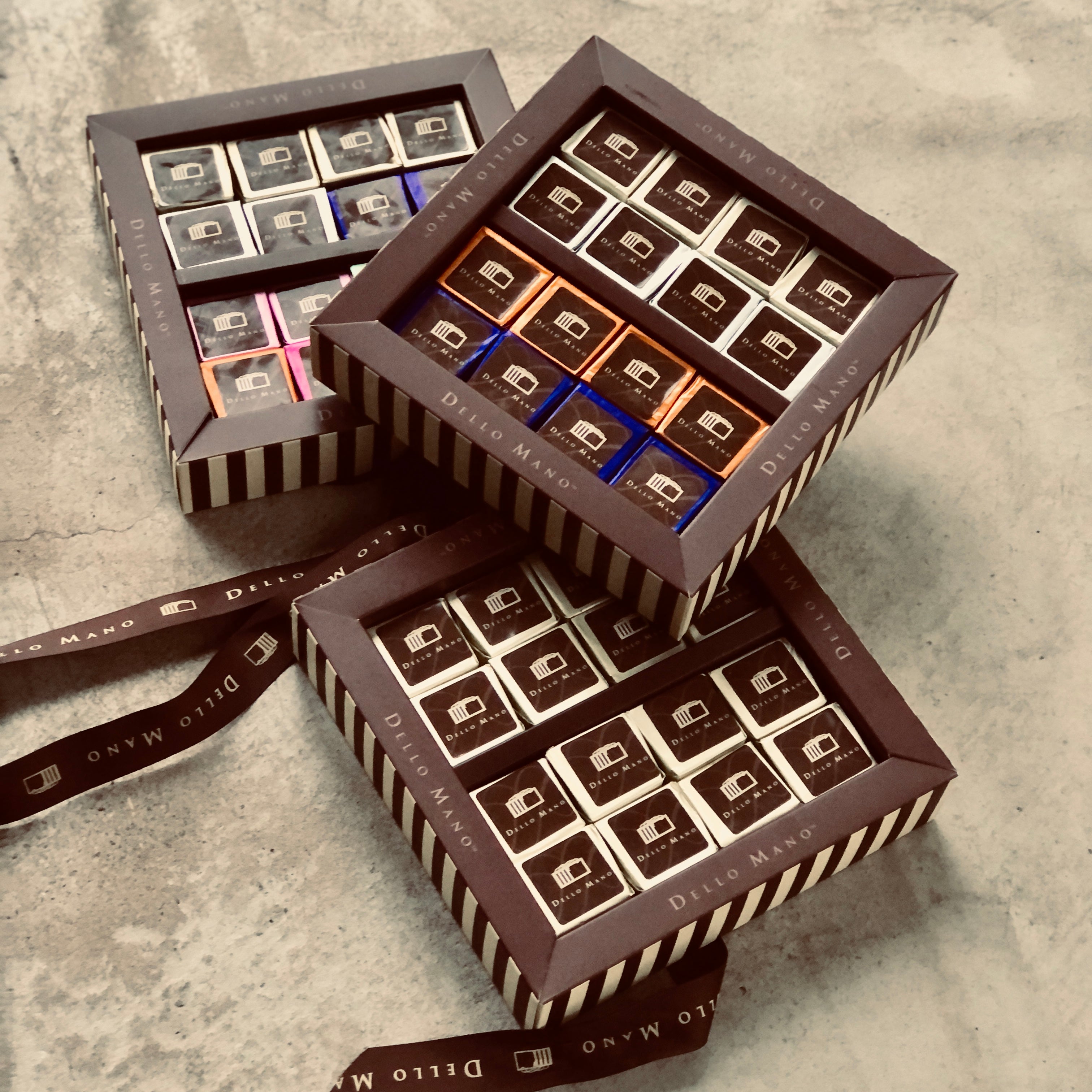 A set of 3 open brownie gift boxes from the Brownie Extravagance Hamper. Each box shows individually foil wrapped brownies each with a logo that says Dello Mano