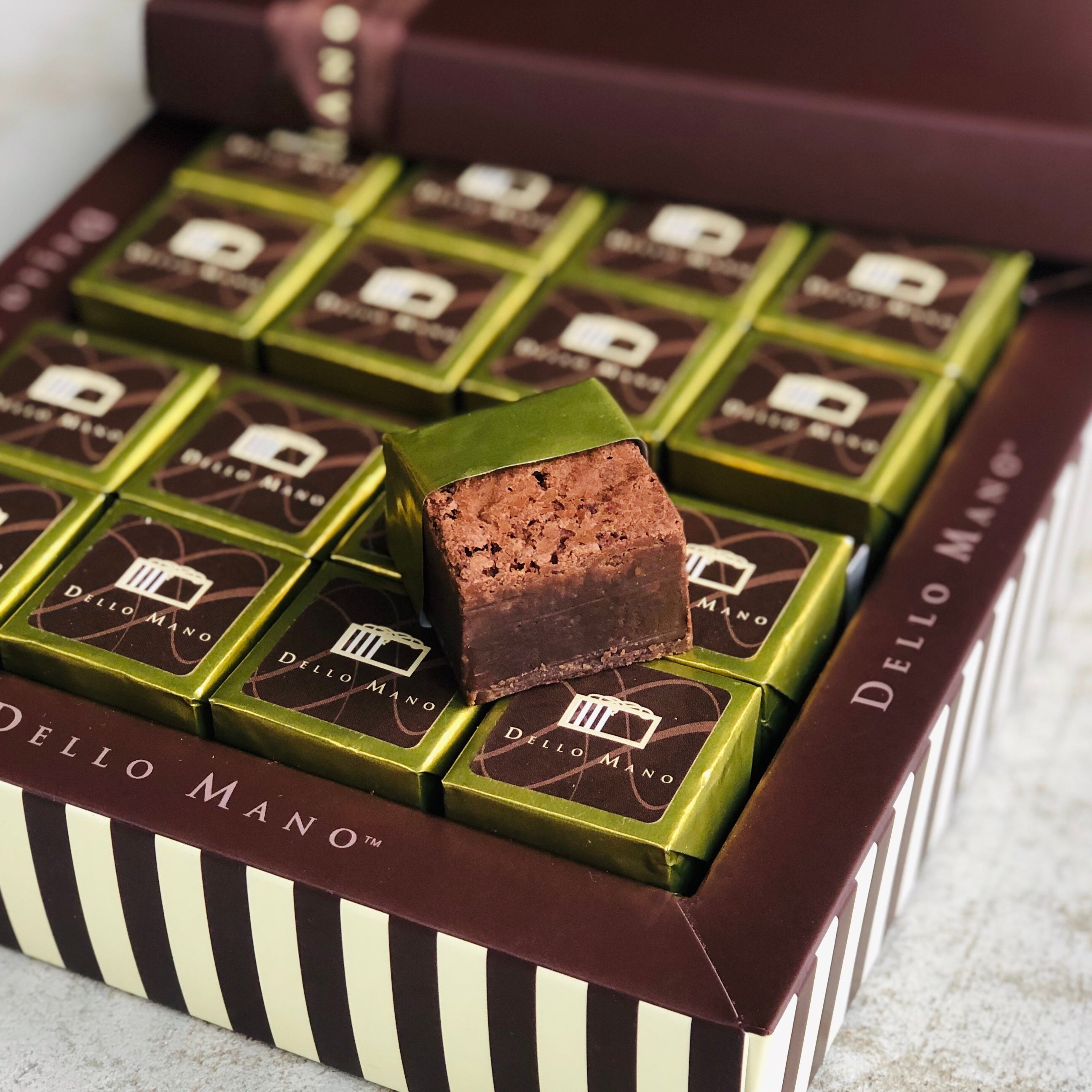 Classic gold foil brownie cubes in a striped chocolate gift box that says Dello Mano. An open foil brownie sits on top