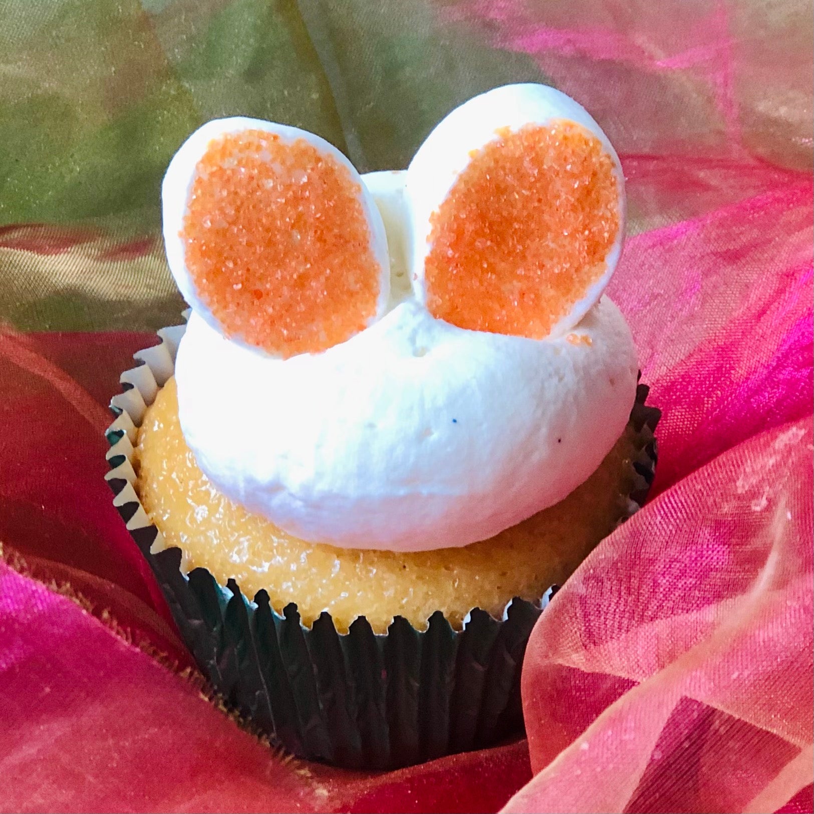 Six Easter Bunny Cupcakes with different coloured ears sitting in front of a cupcake gift box.