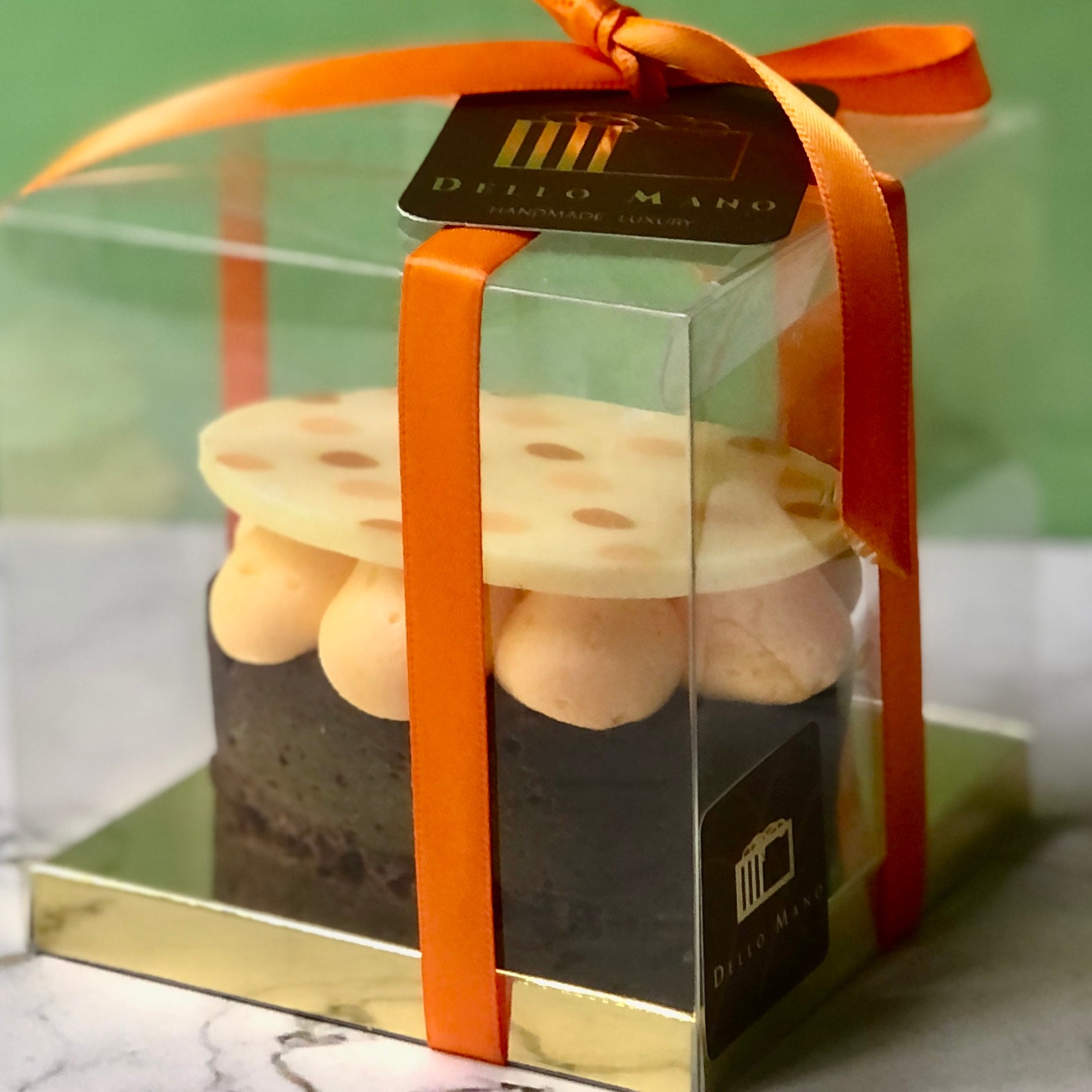 A close  up of an Easter Egg brownie beautifully packaged in a clear gift box finished with orange satin ribbon and a logo that says Dello Mano.