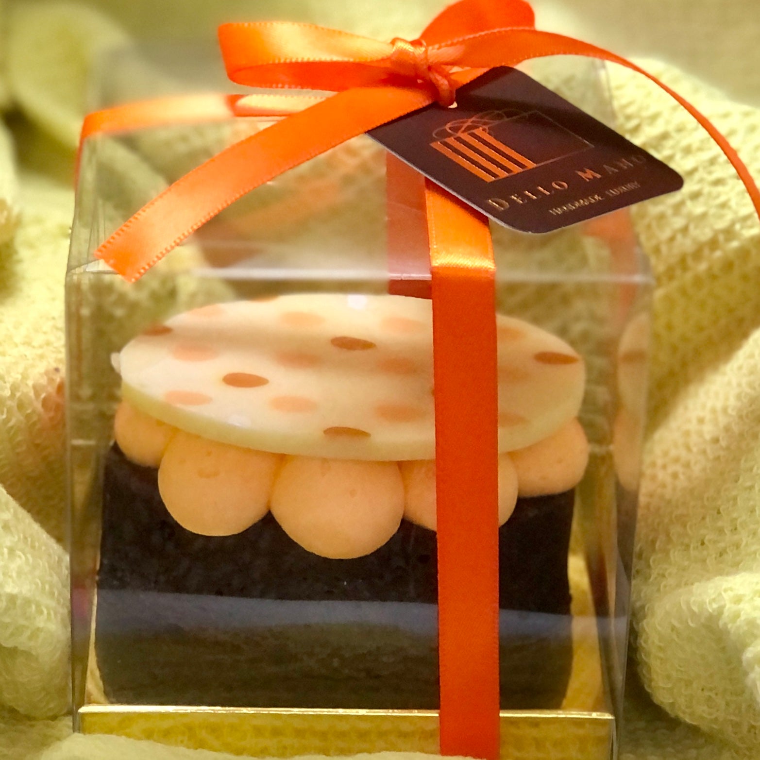 The side view of an Easter Egg Brownie in a gift box. The brownie is topped with pastel orange cream and finished with white chocolate spotted chocolate.