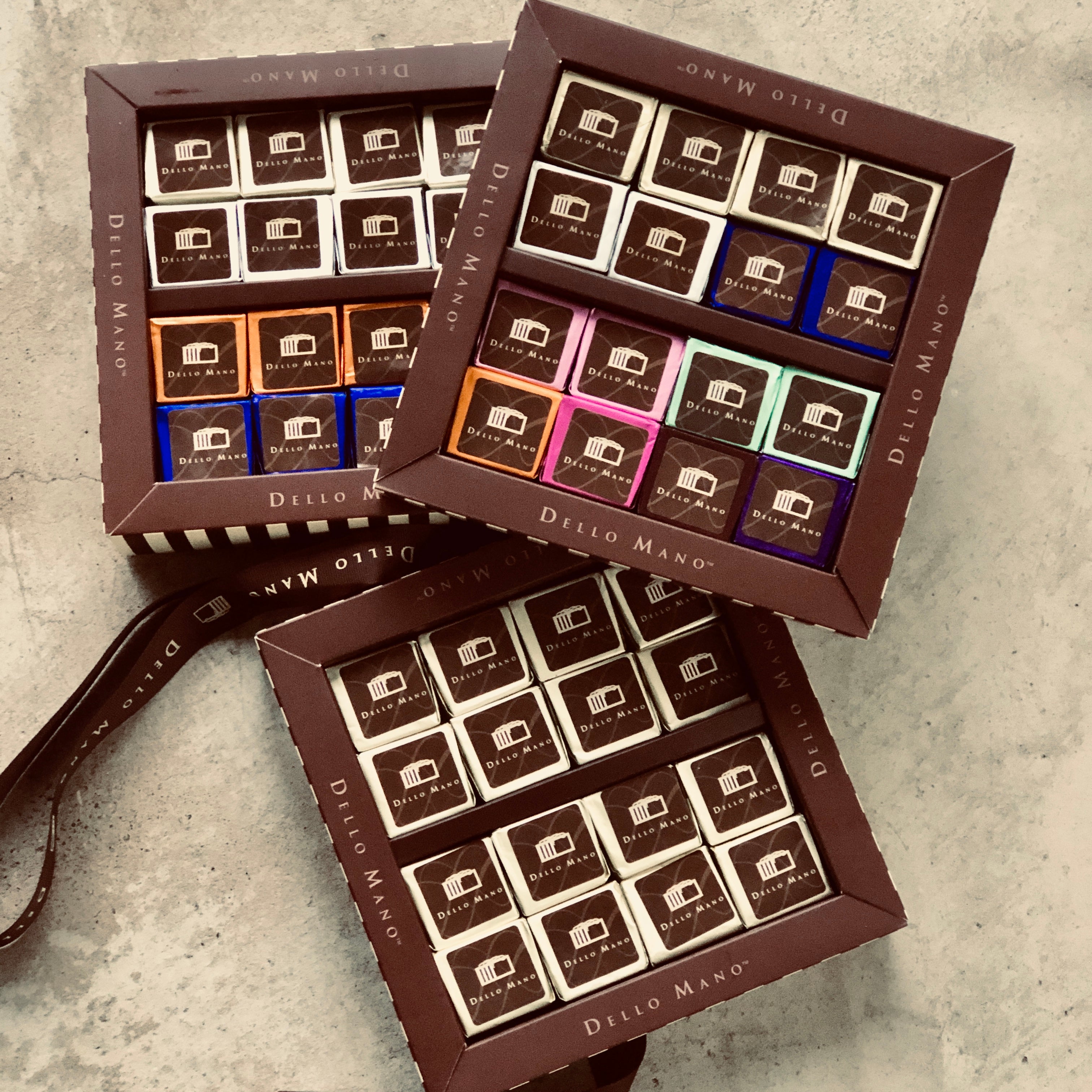 Three Brownie gift boxes each with a different mix of coloured foil brownie cubes. Each individual brownie cube has a label that says Dello Mano