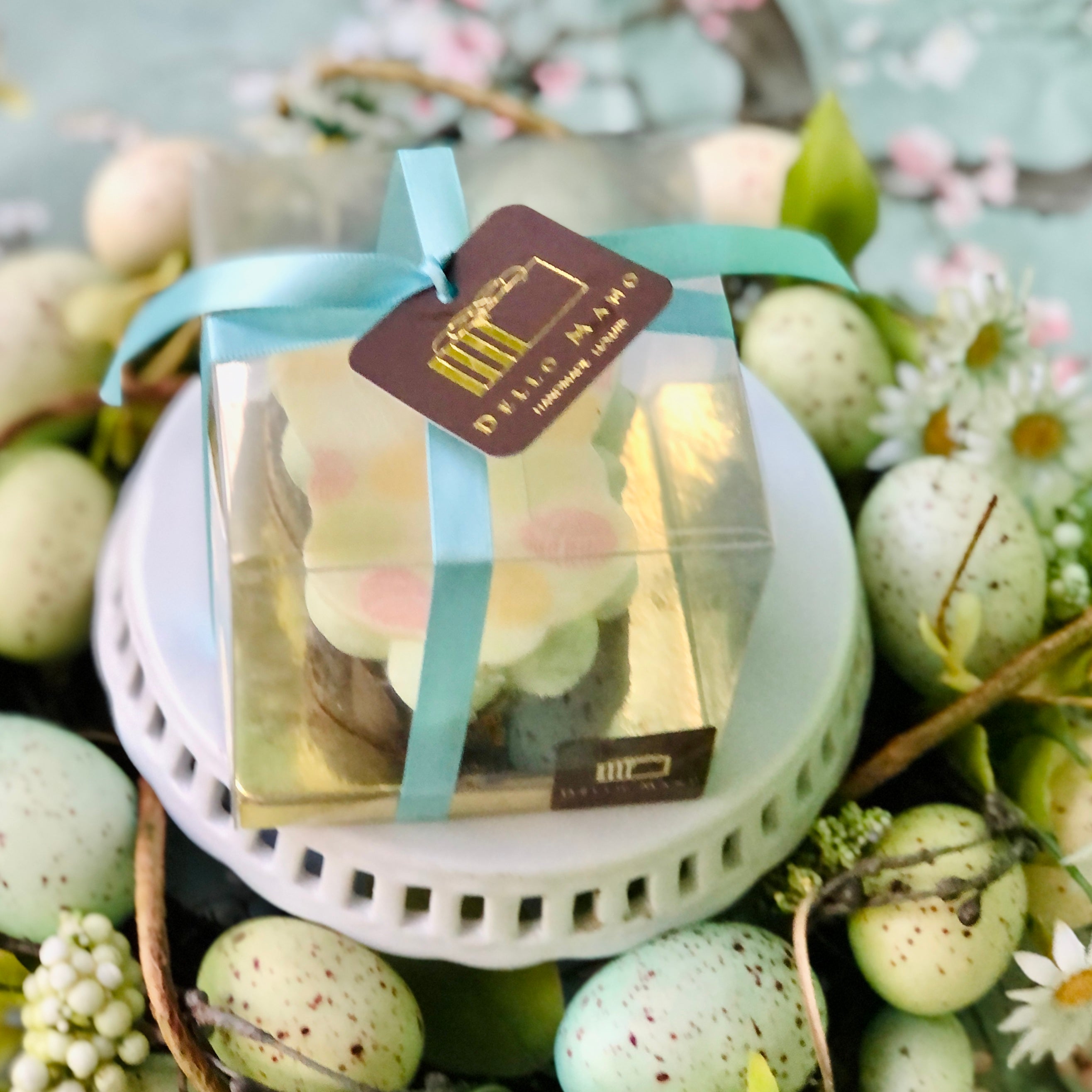 An Easter Brownie Bunny Gift in clear presentation box and finished with blue ribbon. The ribbon has a logo with gold words saying Dello Mano handmade Luxury