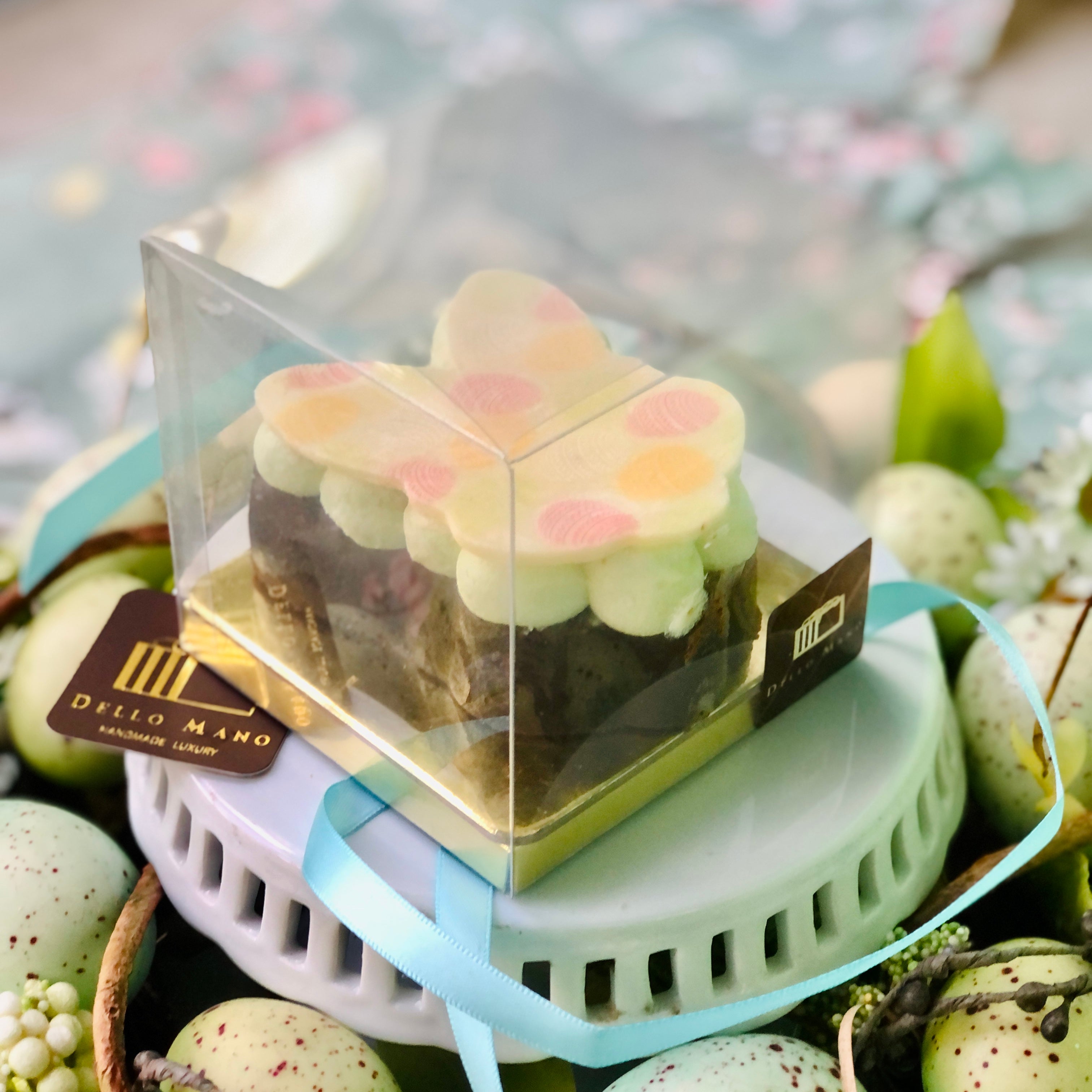 An Easter Brownie bunny in a clear gift box.  A logo with the words Dello Mano is sitting at the side. 
