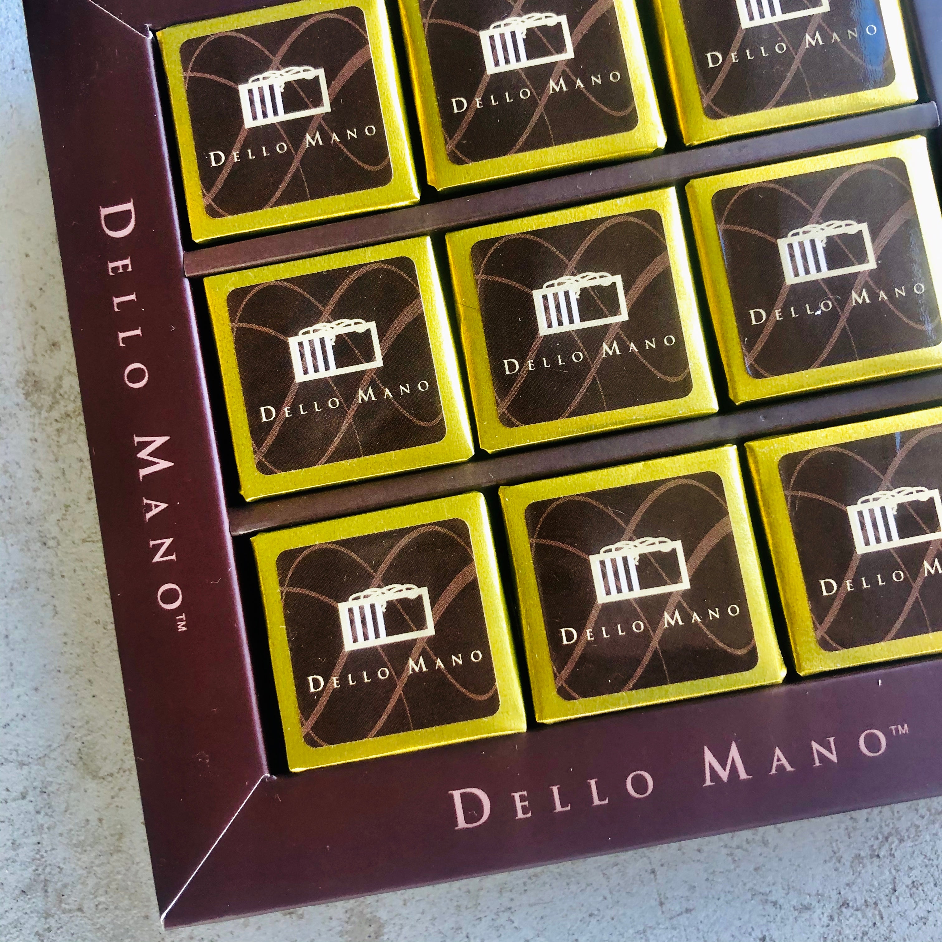 An open Brownie Gift Box showing nine brownies wrapped in gold foil with the words Dello Mano & logo