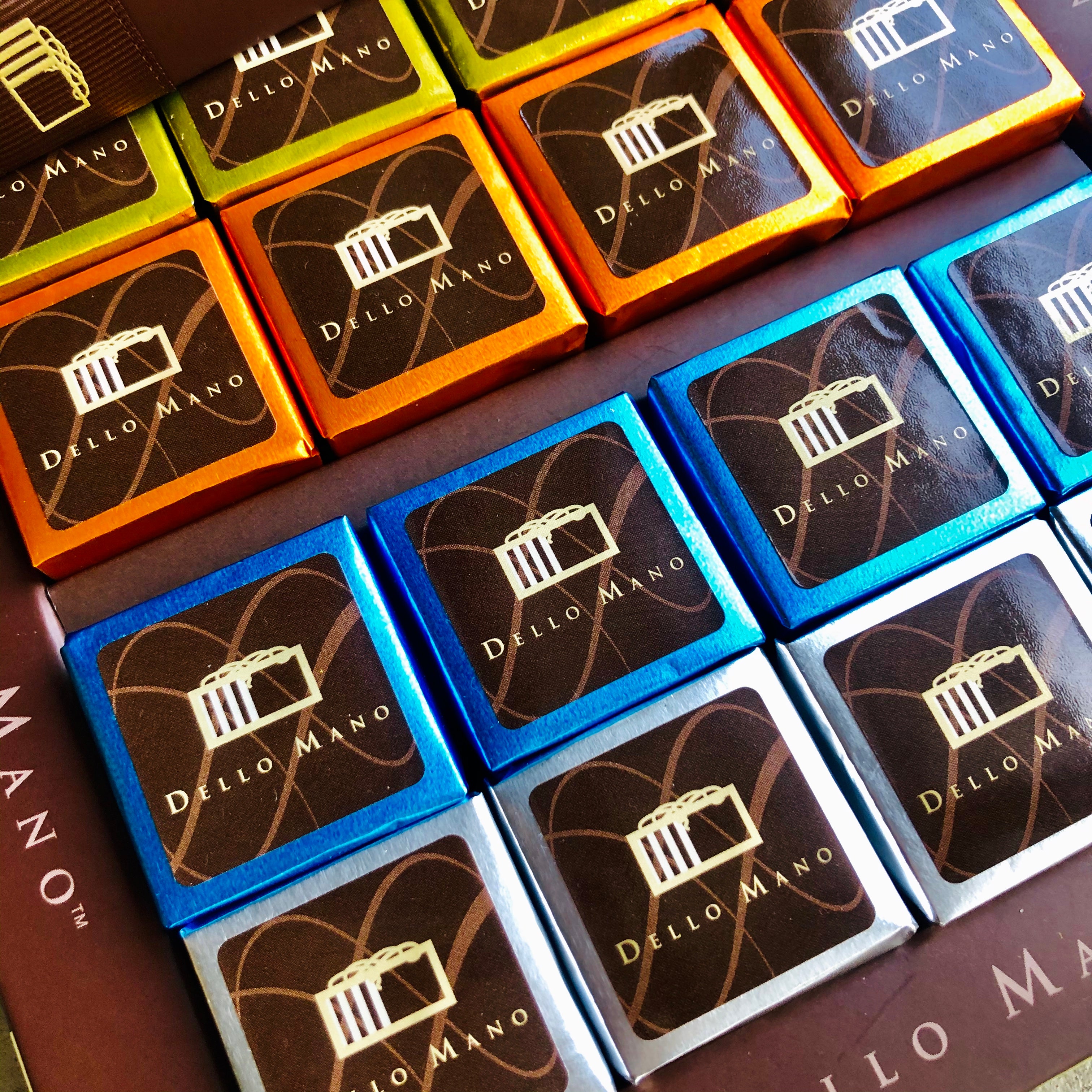 A close up of mixed foiled Brownie cubes. Each brownie has a label that says Dello Mano
