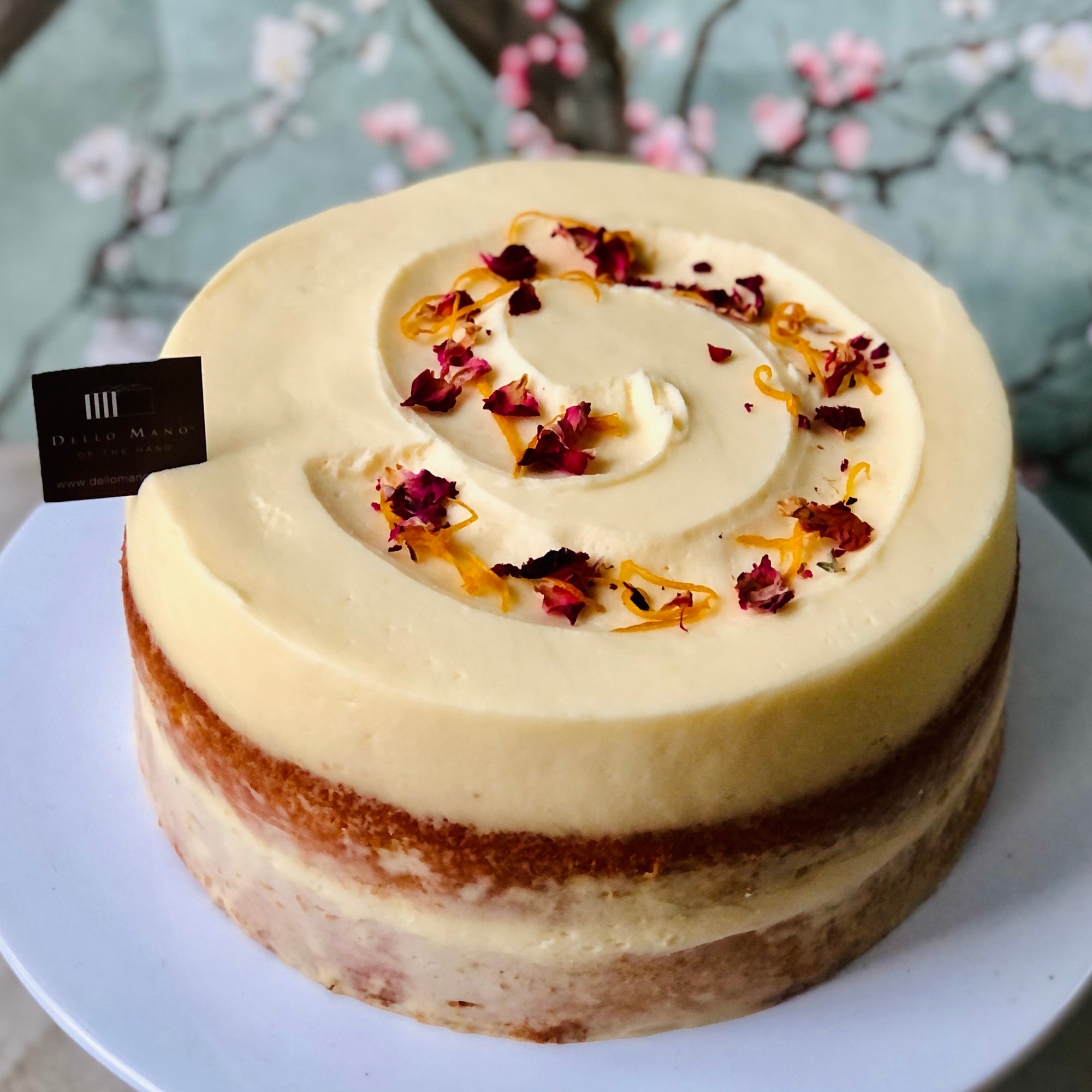 An Orange Almond Cake on a white stand with sprinkles of rose petals and orange zest. 