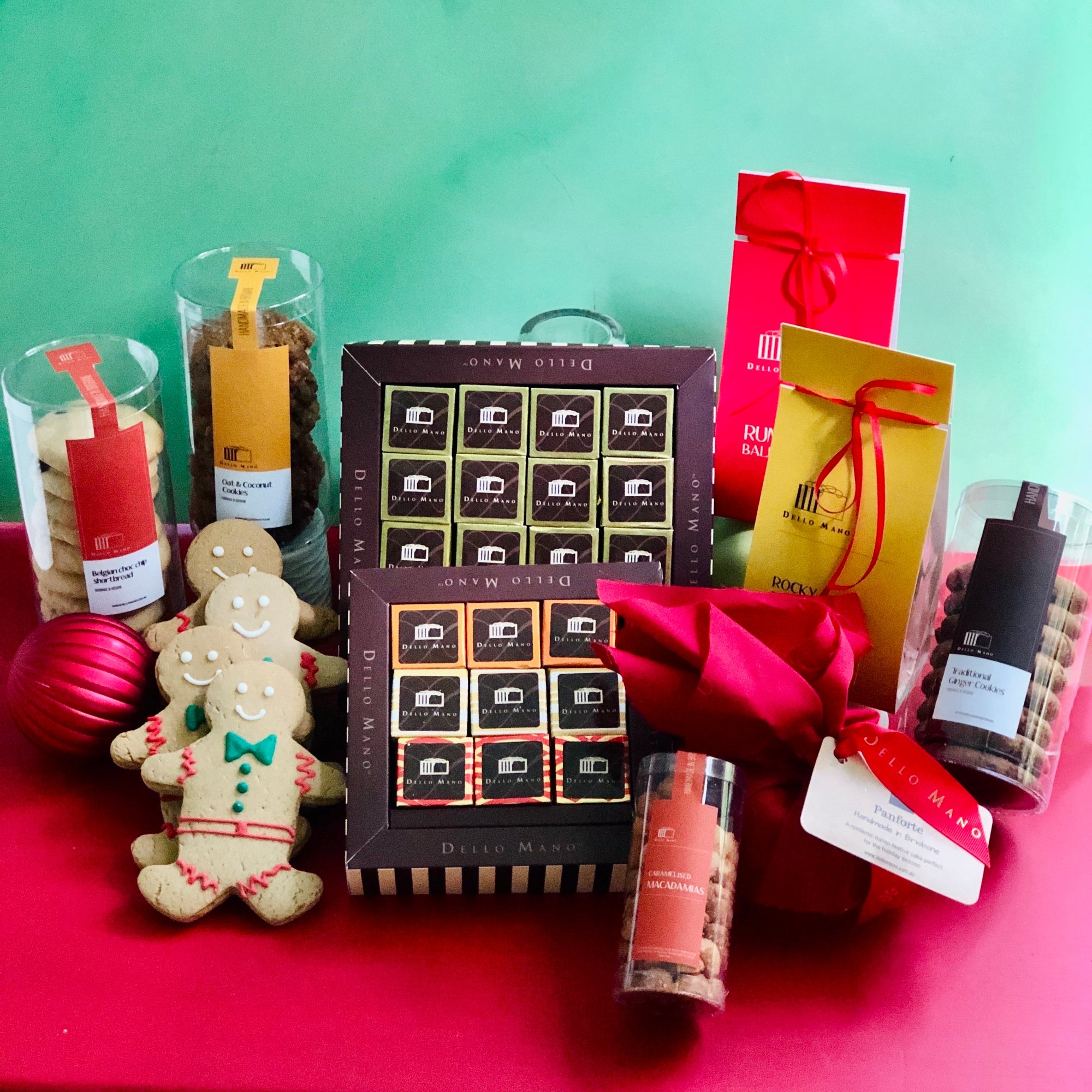 A display of Christmas hamper contents including brownie gift boxes, gingerbread people , tubes of cookies, Rocky road, Rumballs, Panforte and Macadamia nuts. The chocolate gift boxes have a logo that says Dello Mano