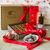 A hamper box with the words printed Dello Mano. In front a gift box of gold foiled brownies, a red bowl of rum balls and a pack of ginger cookies. Two Christmas baubles sit in the forefront of the image. 